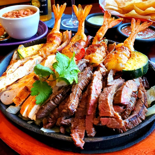Sizzling Maria Rita's Tex-Mex fajitas with chicken, steak, bacon-wrapped shrimp, and vegetables.