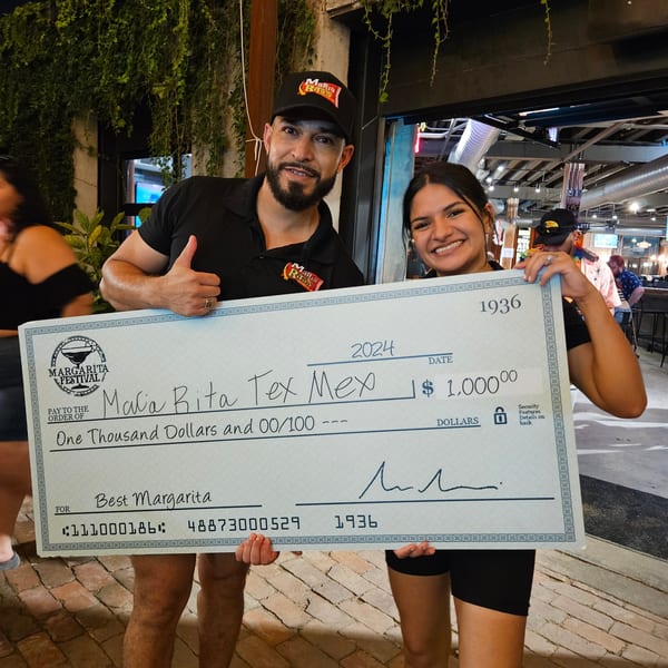 Two smiling people from Maria Rita's Tex-Mex hold a giant check for "Best Margarita" at a festival.