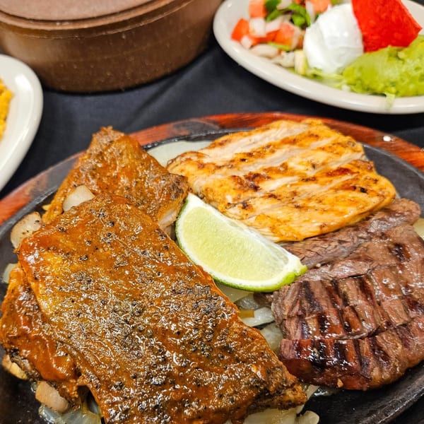 Maria Rita's sizzling fajita platter with grilled chicken, steak, and ribs, garnished with lime.