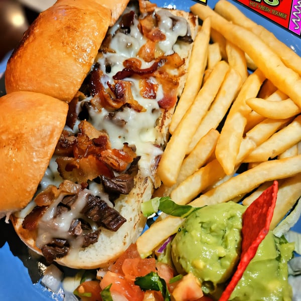 Maria Rita's Tex-Mex cheesesteak with fries, guacamole, and pico de gallo on a blue plate.