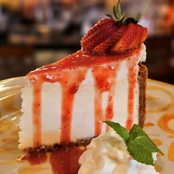 A slice of cheesecake with strawberry topping, whipped cream, and a mint leaf.