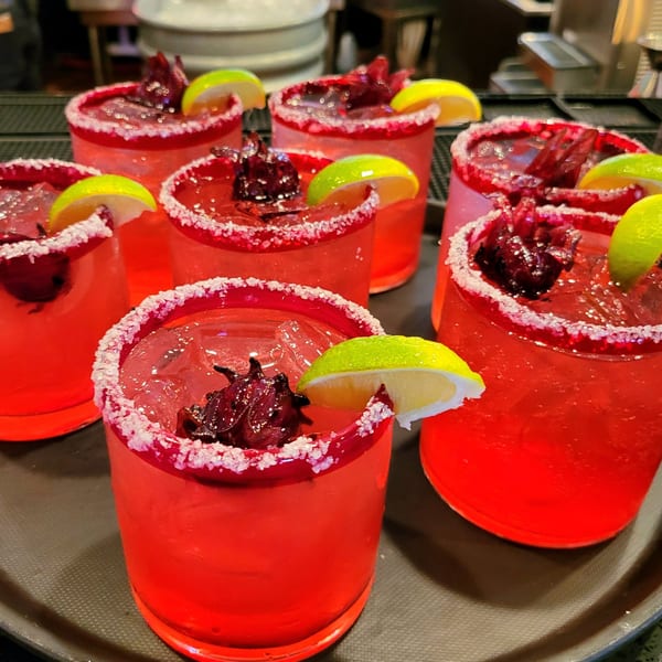 A tray of vibrant red hibiscus margaritas with salted rims and lime wedges at Maria Rita's Tex-Mex.