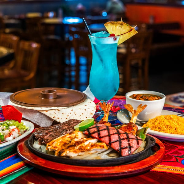 Maria Rita's Tex-Mex fajita platter with steak, chicken, sausage, shrimp, rice, beans, and a blue margarita.